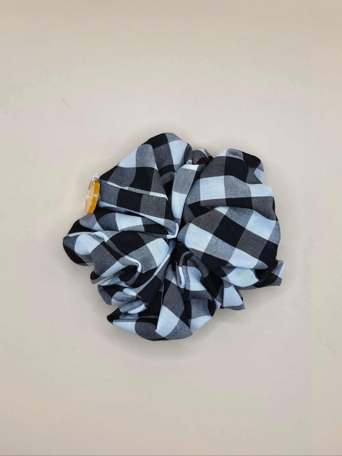 A fabric hair scrunchie with a black and light blue buffalo plaid pattern, shown against a plain beige wall.